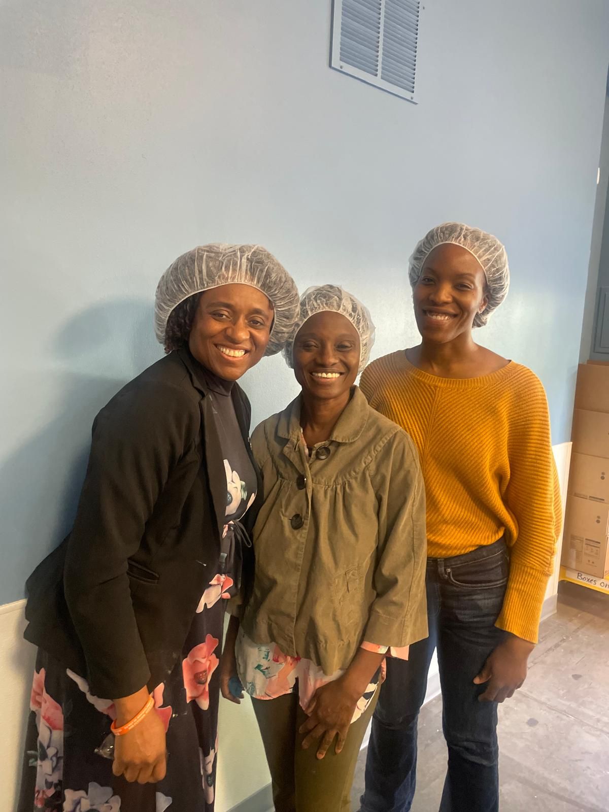 Three ACF Dallas volunteers in hairnets smiling at a food service day